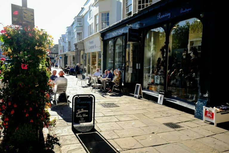 a sidewalk with people sitting at tables and chairs outside of a building