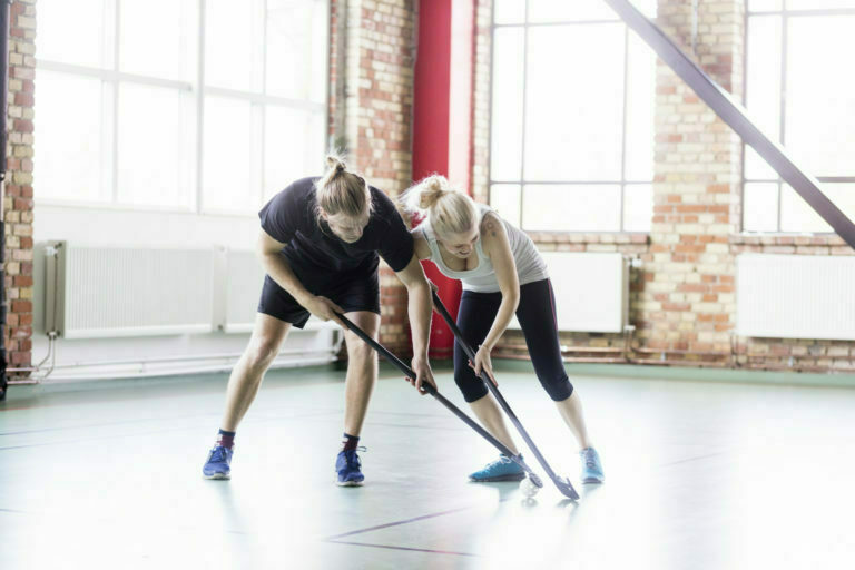 Full length of man and woman playing hockey in health club