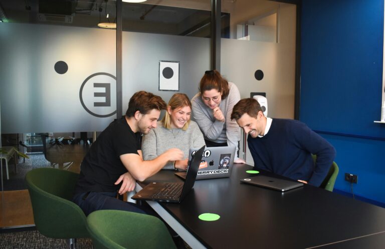 a group of people sitting around a table with laptops